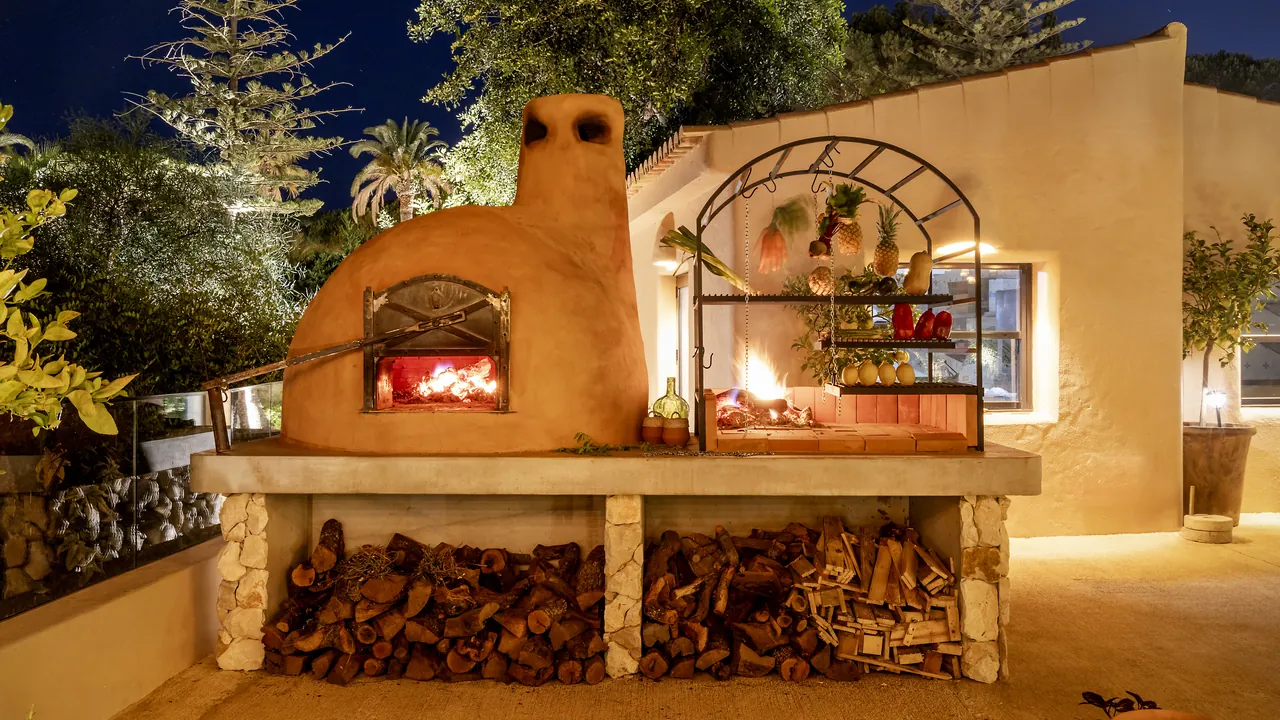 The wood-fired oven at Raízes after dark, lit, with the wood stacked beneath it