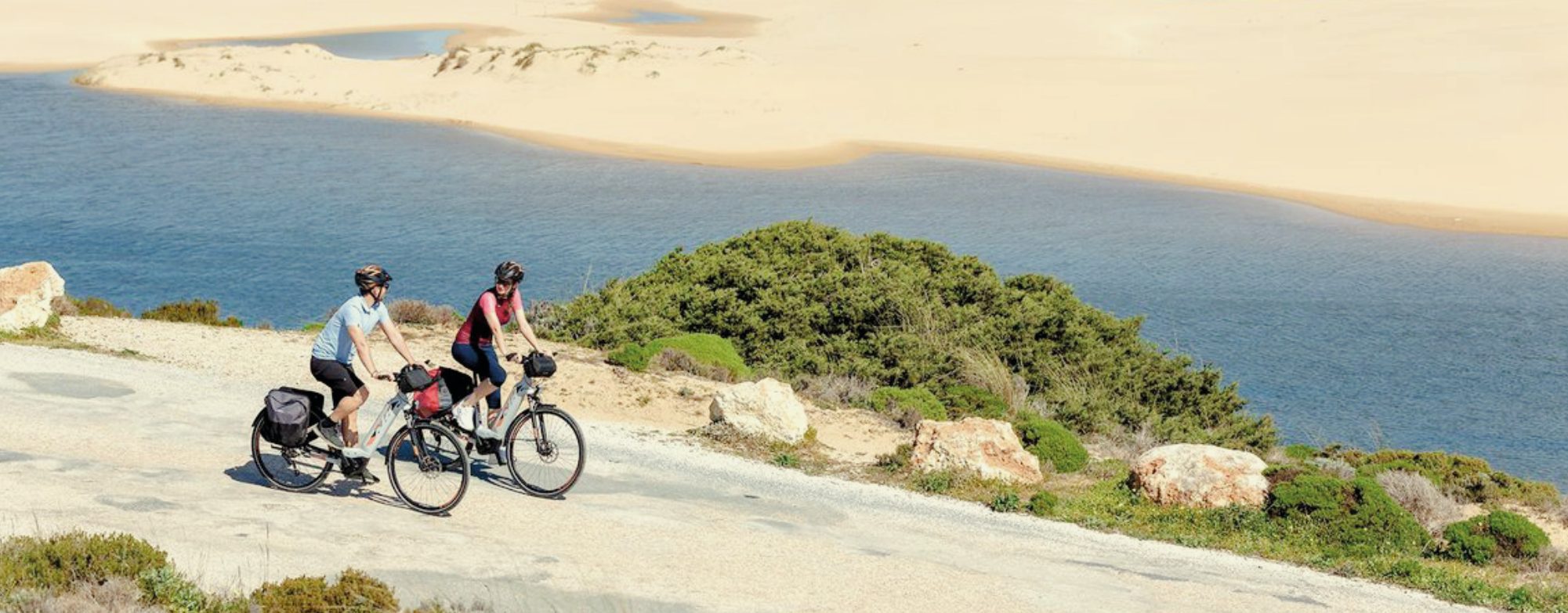 Two people cycling beside a lagoon and the dunes